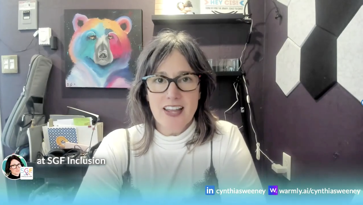 Woman wearing glasses in an office talking and glancing up to her right. A colourful bear painting hangs in the background.